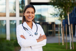Portrait of happy female doctor standing outside at front of modern hospital