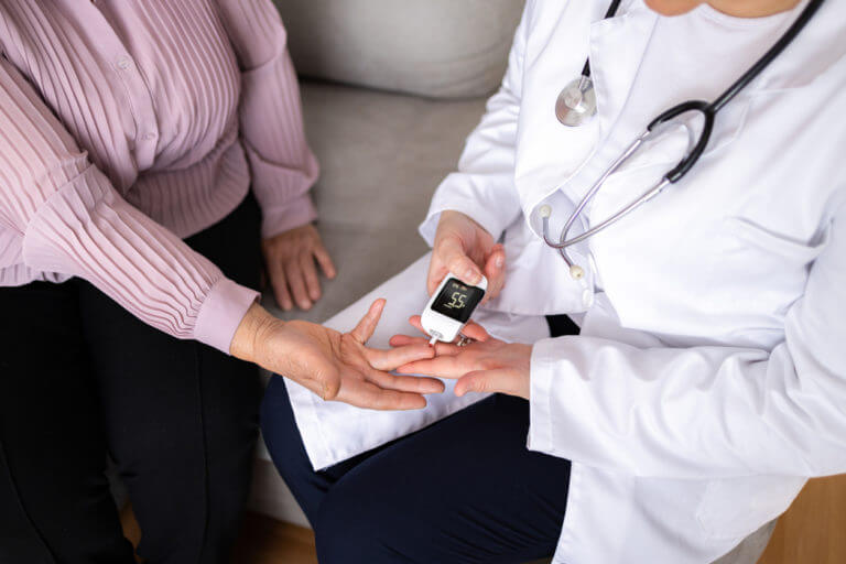 concierge doctor measuring senior female patient blood glucose